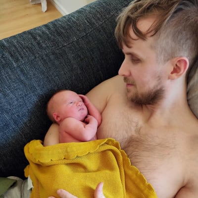 En pappa ligger i soffan med sitt spädbarn på bröstet.