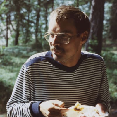Ung man i randig tröja, med mustasch äter tårta utomhus från en papperstallrik. Marit Berndtsons bror Juha.