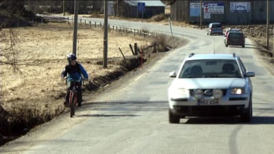 Bil kör om cyklande barn på smal landsväg.