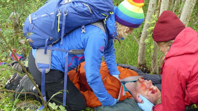 två personer i vildmarken hjälper en tredje som fått en skallskada, simulerd bild