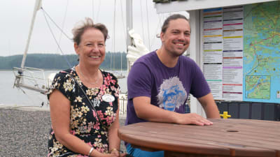 Sonja Petrell-Auvinen och Benjamin Lundin sitter vid ett bord ute. I bakgrunden syns en infotavla och en segelbåt.