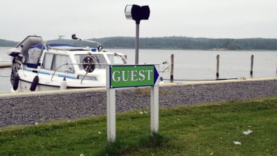 En båt står förtöjd i en gästhamn. I förgrunden syns en grön skylt där det står "guest".