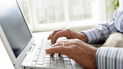 En äldre person sitter och skriver på dator.