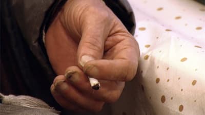 Hand med smuts under naglgarna håller i en cigarettstump. 