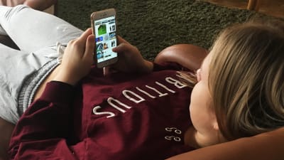 Tyttö löhöää nojatuolissa ja selaa kännykällä Instagramia