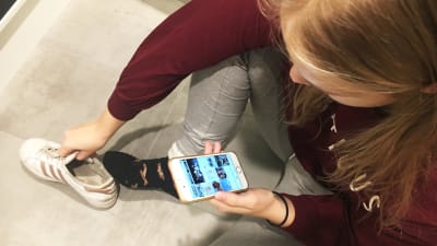 tyttö laittaa kenkiä jalkaan ja selaa samalla Instagramia