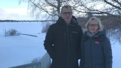 En man och en kvinna med vinterjackor på stårt i ett vinterklätt landskap. I bakgrunden syns bron över Torneälv.