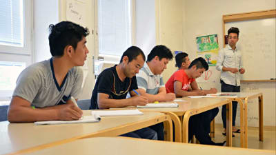 En ung invandrare lär ut finska till andra invandrare i ett klassrum.