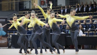 En grupp unga kvinnor i gul-grå gymnastikdräkter står i olika positioner