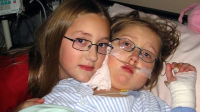 Två barn som ligger i en sjukhussäng. Det ena barnet har bandage på handen och syrgasslang i näsan. 