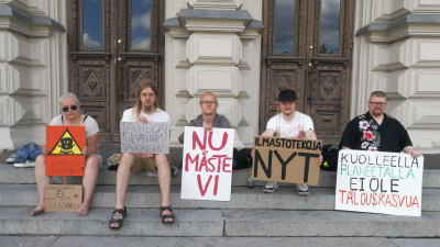 Unga klimataktivister sitter på en trappa med skyltar. 