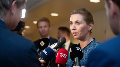 Mette Frederiksen omringad av journalister i Sveriges riksdag.