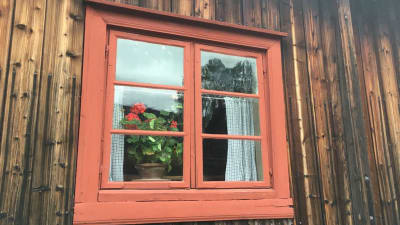 En röd blomma i ett fönster med röda bågar i ett gammalt hus