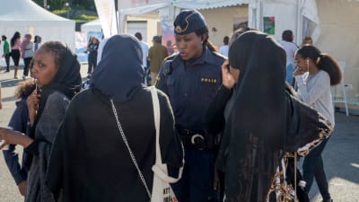 En polis står och pratar om sitt yrke med ett par kvinnor i slöjor. 