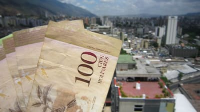 Bolivar-sedlar med värdet 100 från Venezuela. I bakgrunden bild på stad med skyskrapor.