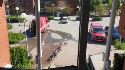 En stor vattenpöl på en parkeringsplats utanför en byggnad.