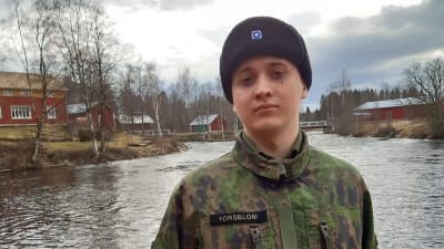 Beväring i militärkläder står framför en tegelvägg.