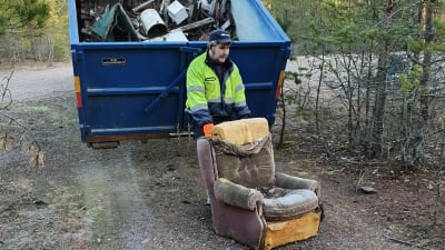 En man med en gammal fåtölj vid en stor skräpcontainer.