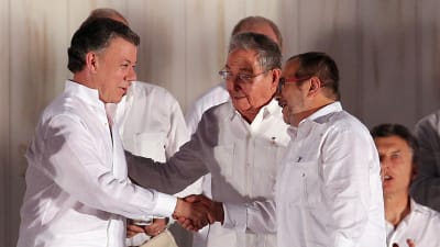 Colombias president Juan Manuel Santos och Farcledaren Rodrigo Londono Echeverri, alias "Timochenko" gratulerar varandra vid underteckningsceremonin. Kubas president Raul Castro följer med i bakgrunden