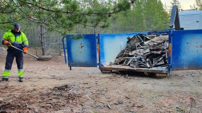 En man städar upp skräp vid en stor container. 