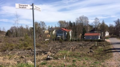 Ett uthugget nytt markområde med äldre hus i bakgrunden.