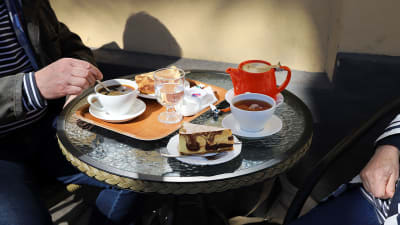 Två personer sitter vid ett kafébord med var sin kaffe och tårtbit.