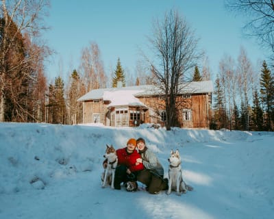 En familj framför ett stort trähus i vinterlandskap.