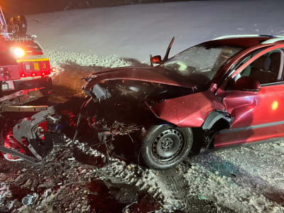 En röd personbil som krockat med en bärgningsbil. Bilens motorhuv är skadad av krocken.