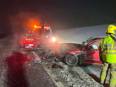 En olycksplats där en röd personbil kört in i en bärgningsbil. På ena sidan står en brandman och inspekterar platsen.