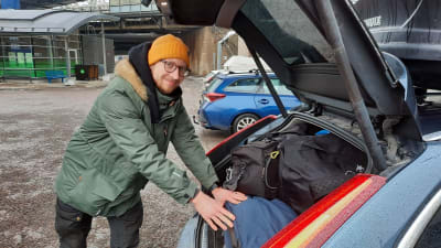Bilisten Eero Jaakkola ikläd en dunjacka och yllemössa skuffar in sportväskor i bilens baklucka.