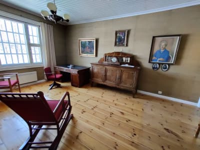 Ett museum som visar Miina Sillanpääs arbetsrum med gungstol, skrivbord, byrå och hennes porträtt på väggen.