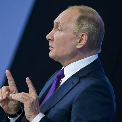 President Vladimir Putin sitter bakom två mikrofoner och med pekfingrarna utsträckta.