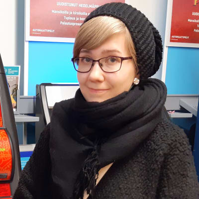 Nuori nainen seisoo kaupan rahapeliautomaattien edessä ja hymyilee.
