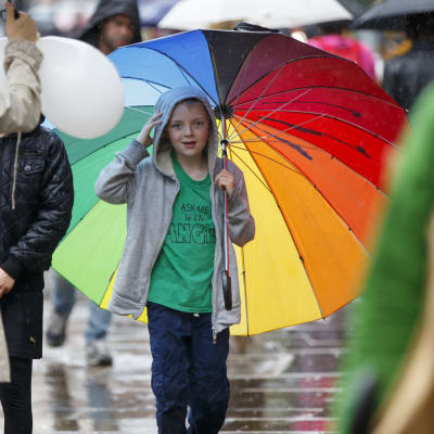 En pojke håller i ett regnbågsfärgat paraply medan han går ute i regnet.