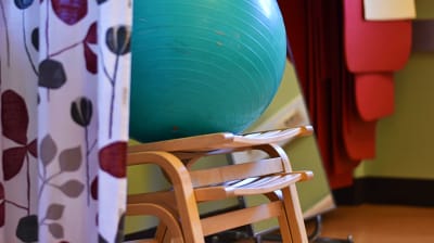 En gymnastikboll på några stolar som står radade. Bredvid hänger några yogamattor.