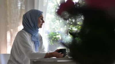 En kvinna vid ett fönster som håller en kopp i handen.