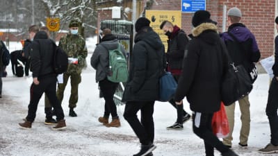 Personer som vandrar in genom porten vid Nylands brigad. Det är vinter och alla bär munskydd.