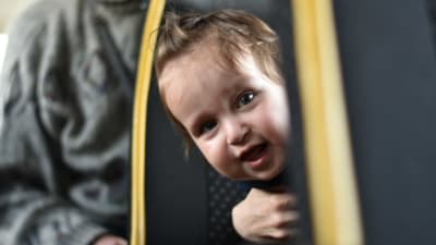 En liten pojke på ett år kikar fram mellan bussäten och ler.