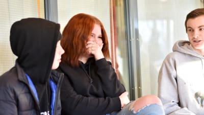 Tre ungdomar sitter och pratar i en skolmiljö.