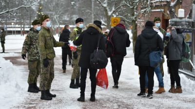 Många personer köar utanför porten till Nylands brigad. Det är vinter och alla bär munskydd.