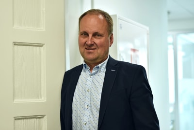 Man i skjorta och kostym står lutad mot en vit trädörr.