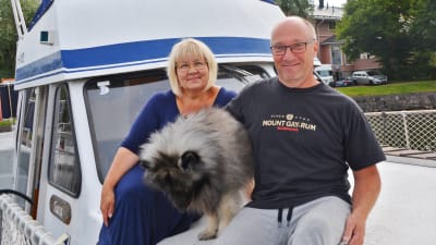 En kvinna, en man och en hund sitter utanpå en blåvit båt i Borgå gästhamn.