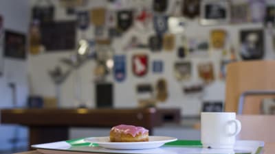 En bricka med en kaffekopp och en munk med ljusröd glasyr.