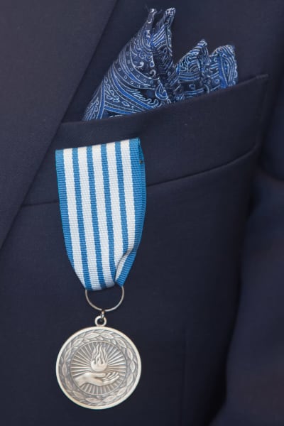 En silverfärgad medalj i ett blåvitt band som är fäst vid bröstfickan på en kavaj.