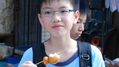 En kinesisk pojke med glasögon håller i kanderad frukt spetsad på en pinne.