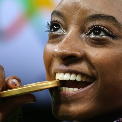 Simone Biles biter på sin OS-guldmedalj.