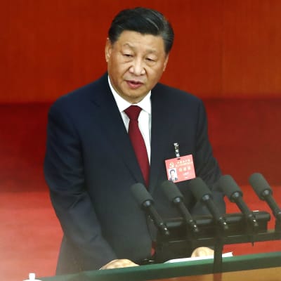 Pukuun pukeutunut Xi Jinping seisoo puhujakorokkeella ja katsoo hieman vasemmalle.