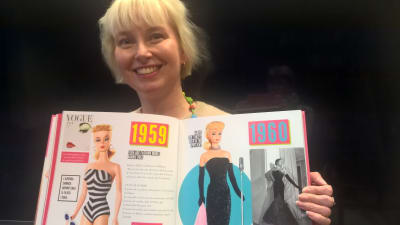 Utställningschef Minerva Keltanen håller i en stor bok om Barbiedockan.