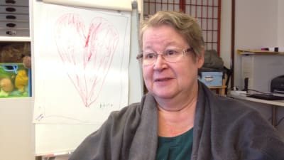 medelålders kvinna med glasögon sitter vid en tavla