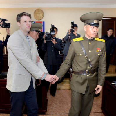 Kuvassa surullinen Otto Warmbier, jota vetää kädestä pohjoiskorealainen sotilas.